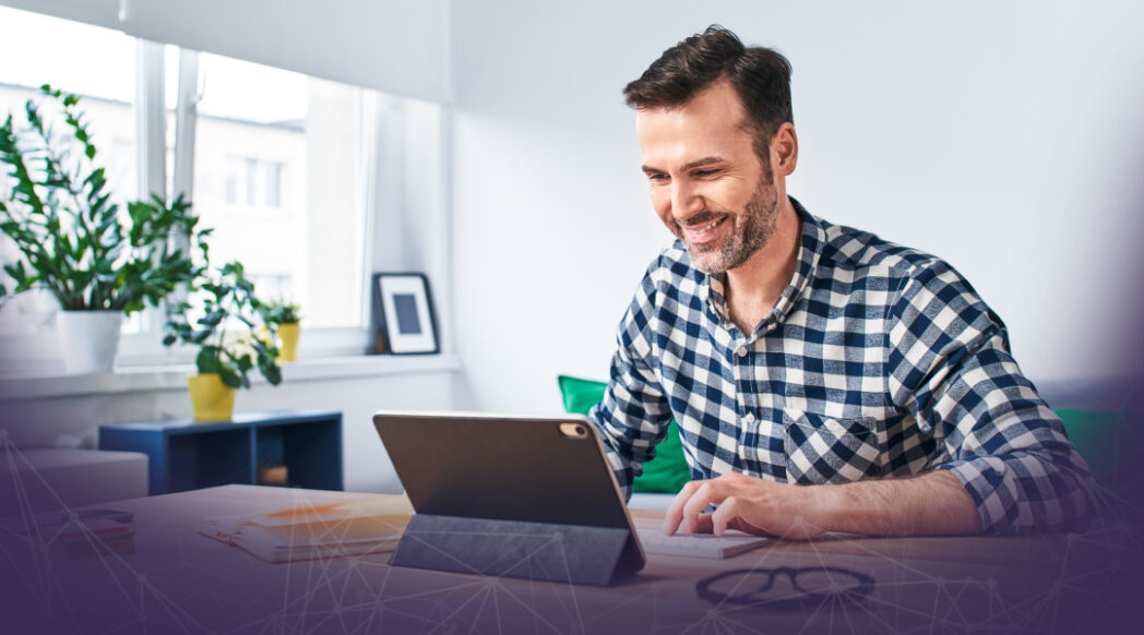 Man in a tshirt smiling looking at a tablet working from home